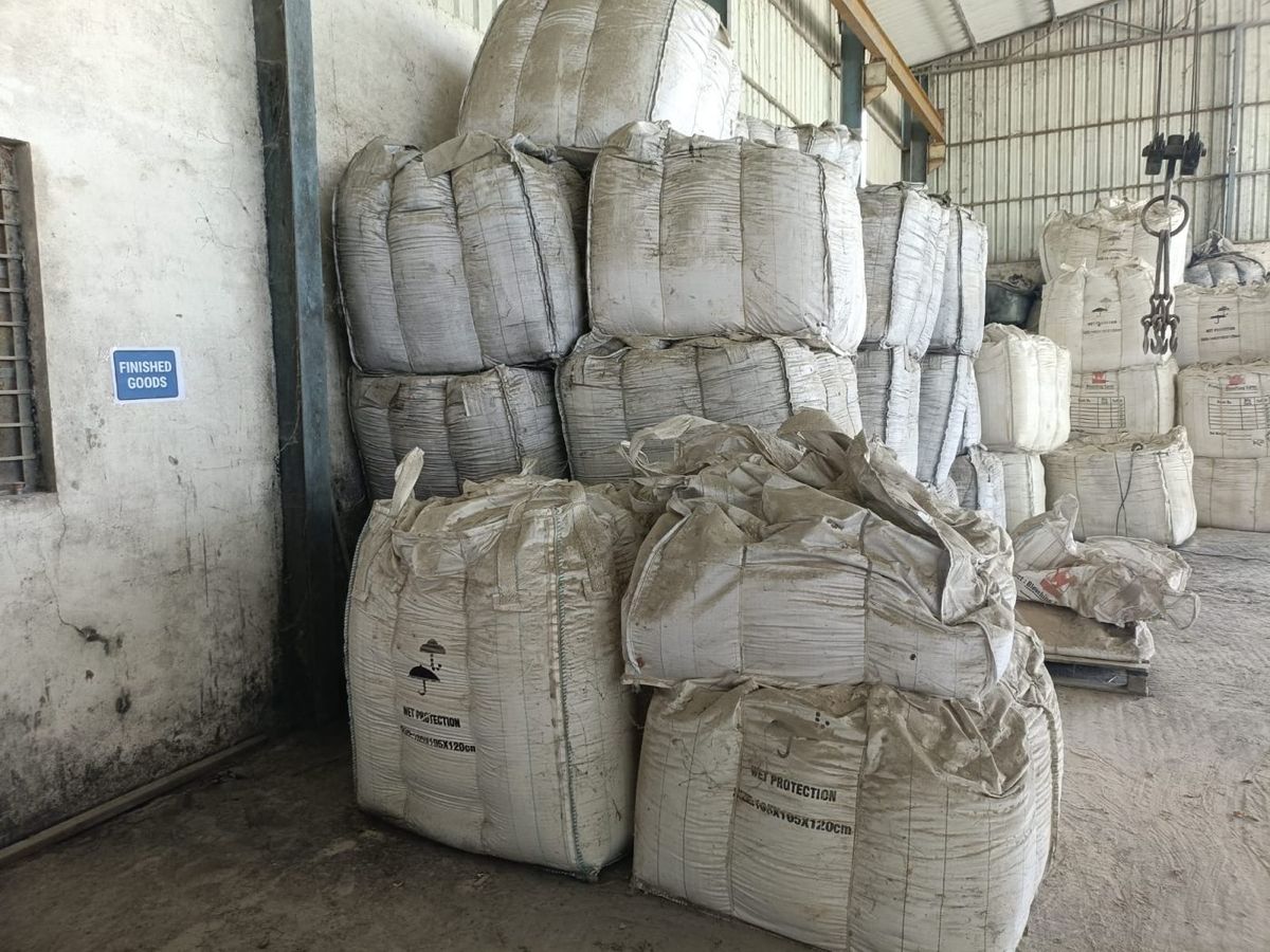 Bags stacked against a wall beside a sign reading Finished Goods. The bags carry printed panels for batch number, manufacturing date and net weight.