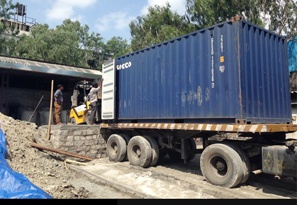 A blue shipping container on a trailer, doors open at the near end, a forklift standing beside it.