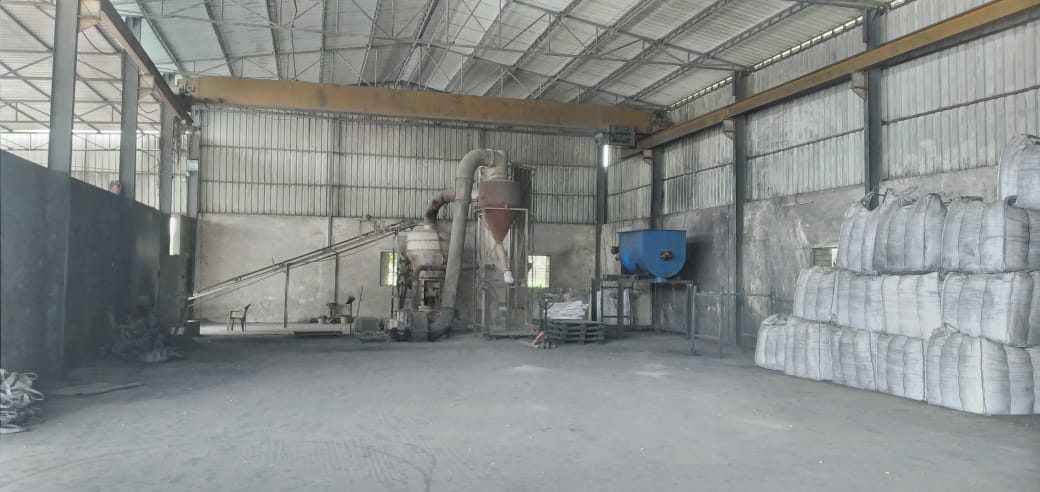 Inside the mill shed: a pulveriser with cyclone separator and feed conveyor, filled bags stacked along the far wall.